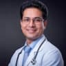 Confident Indian male doctor in white coat with stethoscope offering medical consultation